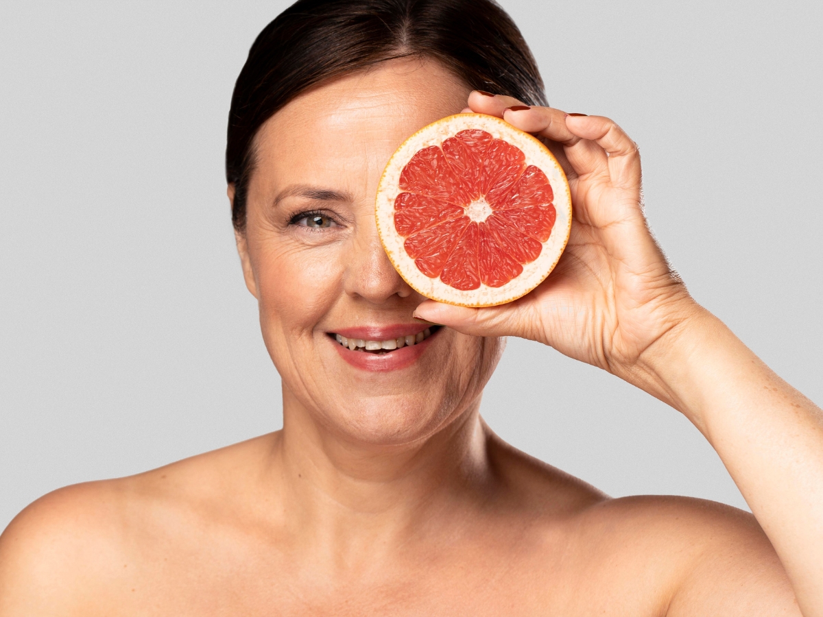 Mujer de 55 años con piel uniforme sostiene una toronja mostrando la relación de la comida y la piel. 